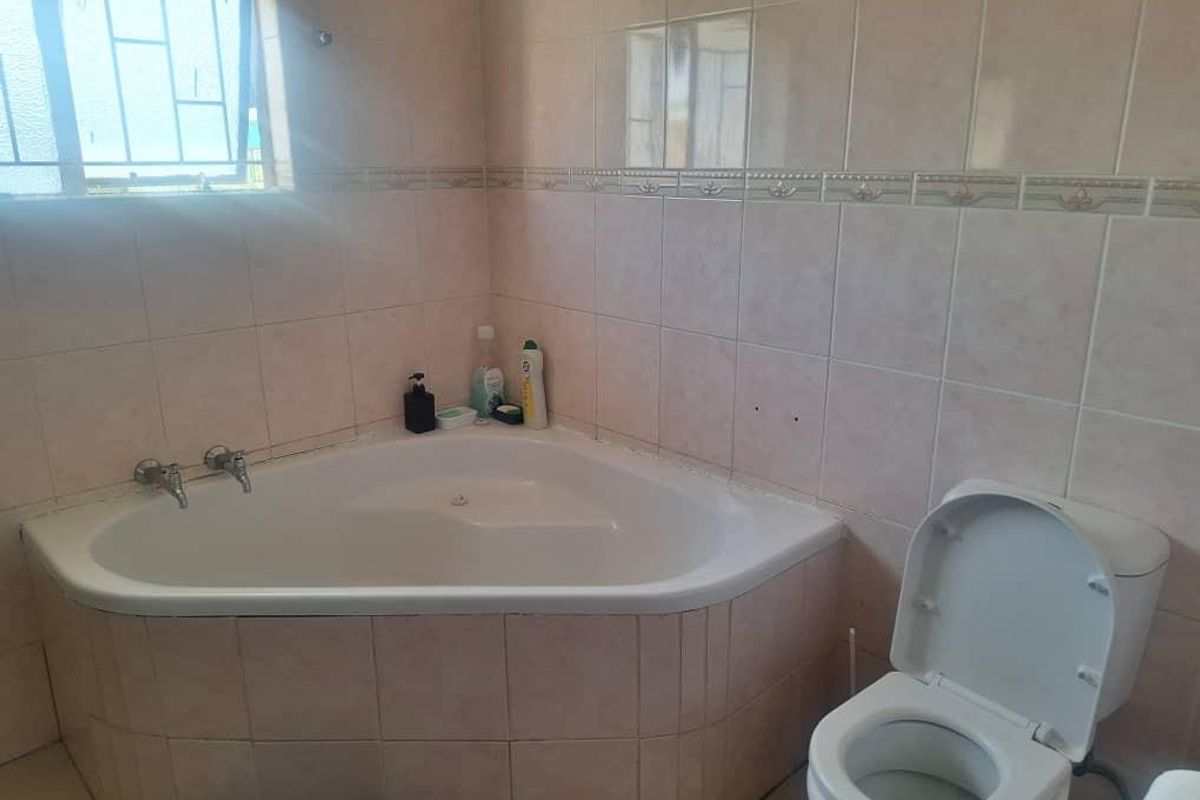 A functional bathroom featuring a corner bathtub, a standard toilet, and tiled walls. The space requires minor maintenance and cosmetic updates.