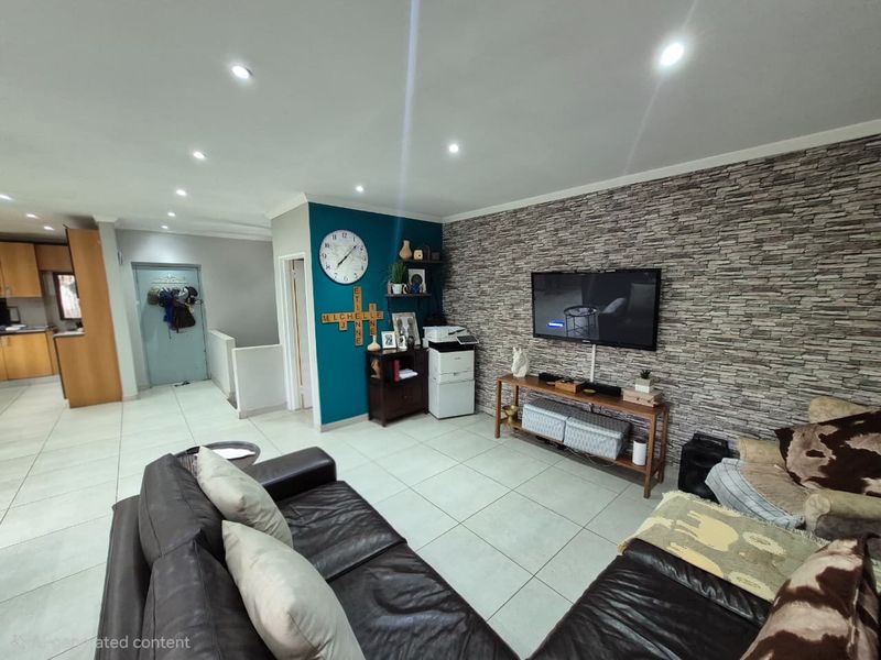 An open-plan living area featuring a stone veneer accent wall, recessed downlighting, and neutral tiled flooring, seamlessly connecting to the adjacent kitchen space.