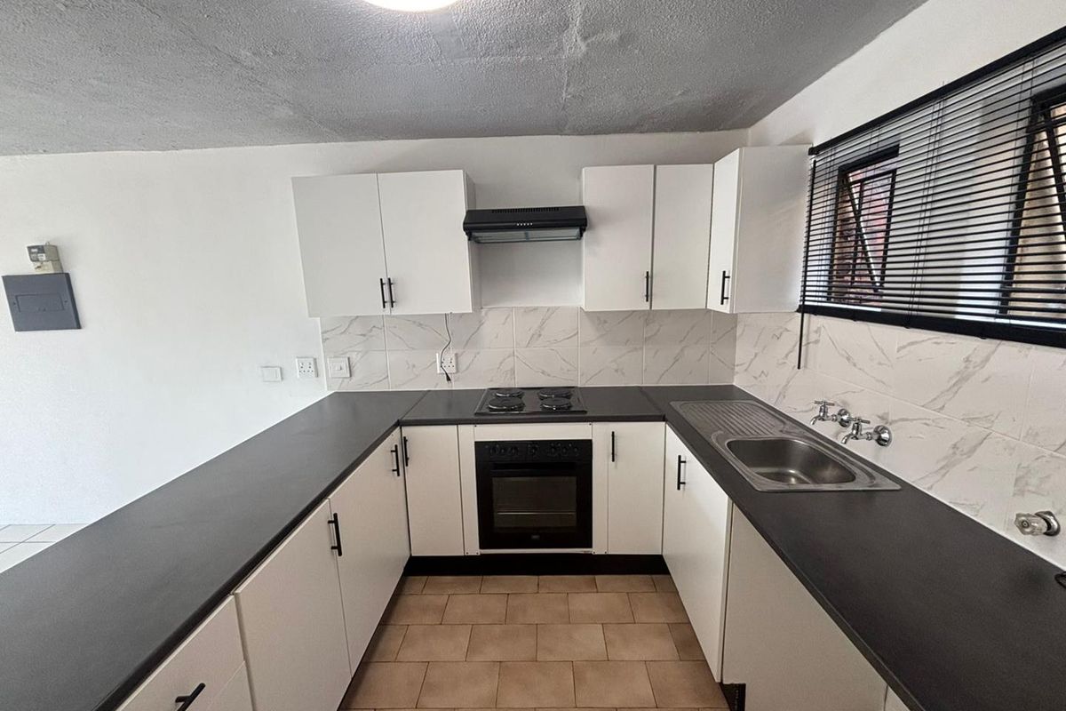 A functional kitchen featuring white cabinetry, dark countertops, built-in oven with hob, extractor fan, and tiled backsplash.