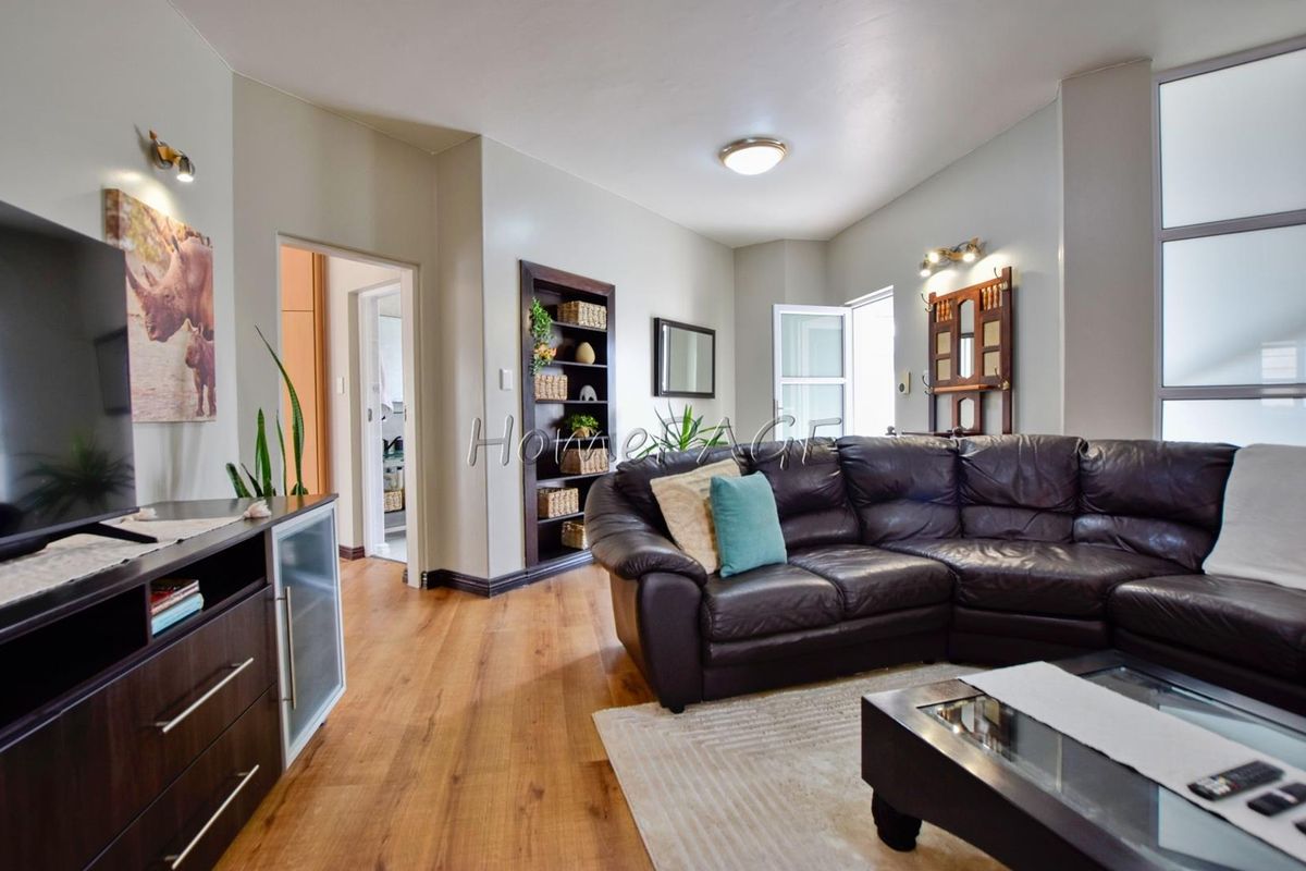 A well-maintained living room featuring warm wood-look flooring, neutral wall tones, and access to adjacent rooms, providing a comfortable and functional living space.