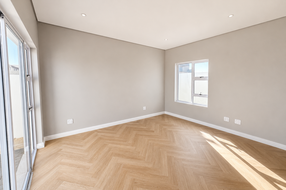 A bright, empty bedroom featuring modern herringbone wood-look flooring, neutral walls, recessed ceiling lighting, and large sliding glass doors leading to the exterior.