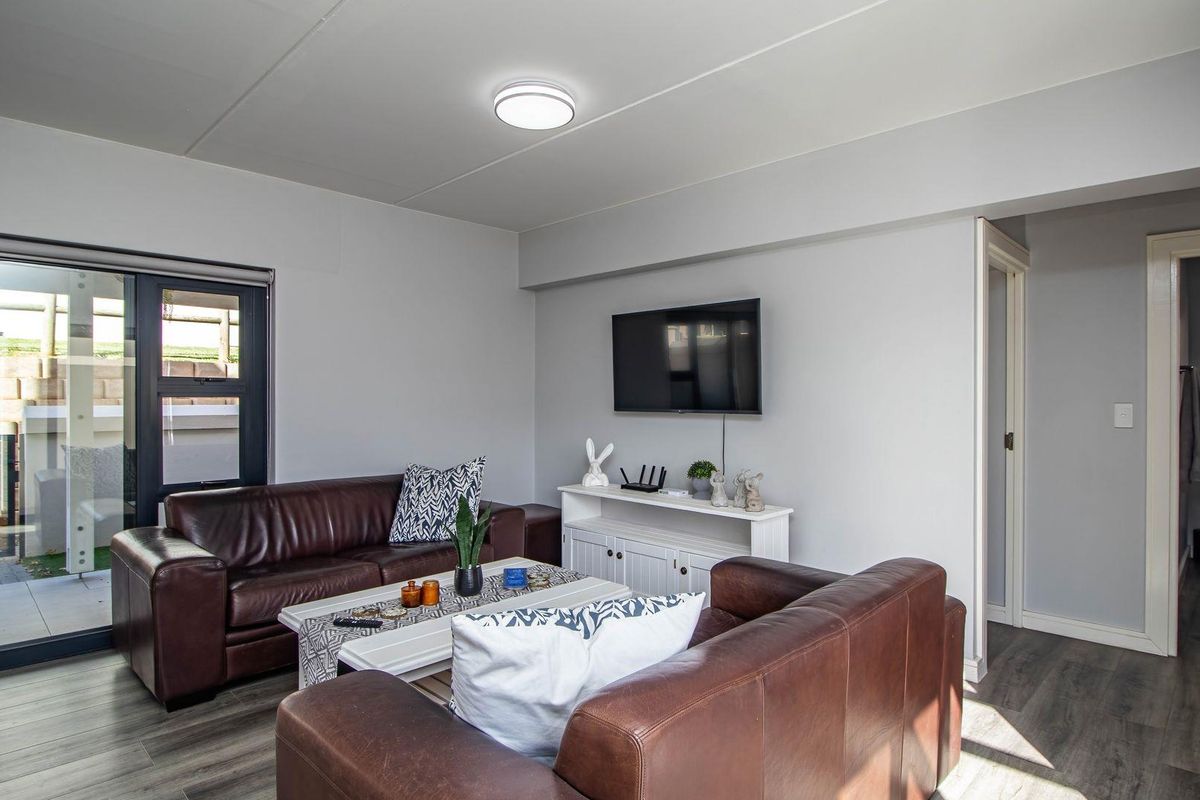 A well-maintained living room featuring modern wood-look flooring, neutral walls, and a sliding glass door providing access to an outdoor patio area.