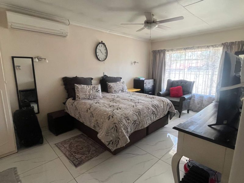 A spacious bedroom featuring tiled flooring, a built-in wardrobe, a ceiling fan, and a wall-mounted split-system air conditioner for climate control.