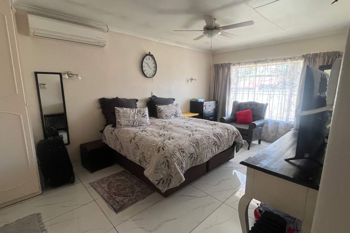 A spacious bedroom featuring tiled flooring, a built-in wardrobe, a ceiling fan, and a wall-mounted split-system air conditioner for climate control.