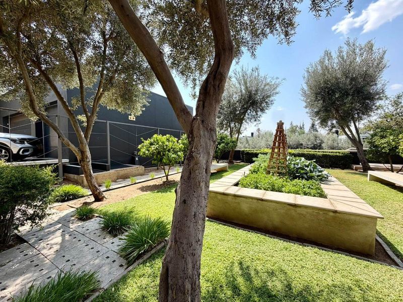 A well-maintained garden featuring raised planting beds, paved walkways, and mature trees adjacent to the modern townhouse exterior.
