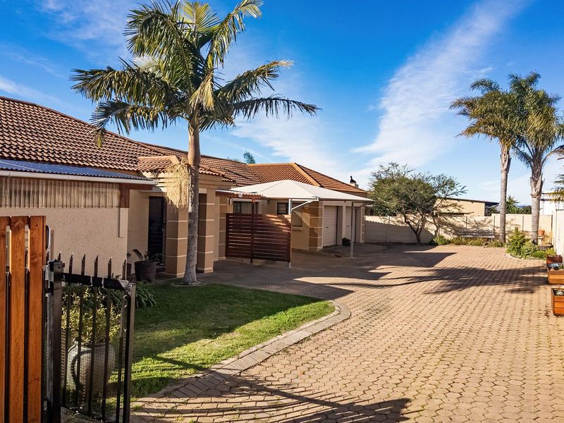 Front exterior view of the townhouse featuring a paved driveway, carport, and well-maintained boundary walls with established palm trees.