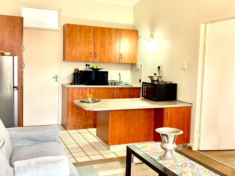 Open-plan living area featuring a compact kitchen with laminate cabinetry, stone-look countertops, and tiled flooring, seamlessly integrated with the living space.