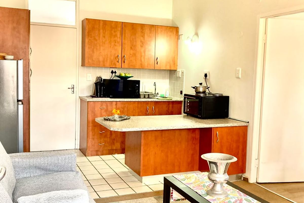 Open-plan living area featuring a compact kitchen with laminate cabinetry, stone-look countertops, and tiled flooring, seamlessly integrated with the living space.