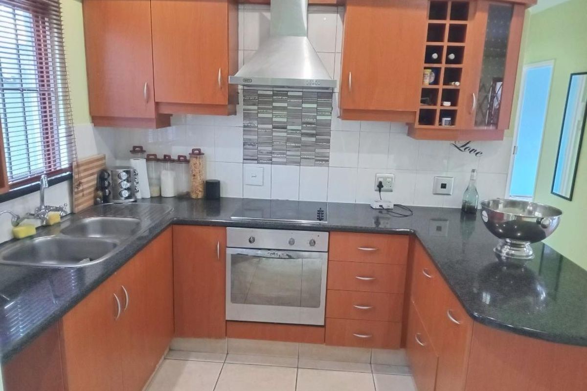 A functional U-shaped kitchen featuring wooden cabinetry, granite countertops, a built-in oven, and a stainless steel extractor fan.