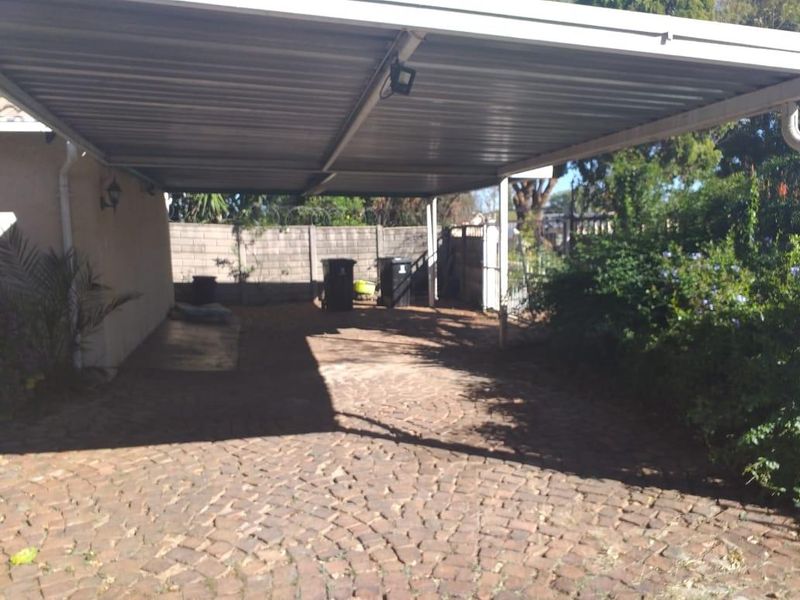 A covered carport area featuring paved flooring and a secure perimeter wall, providing sheltered off-street parking.
