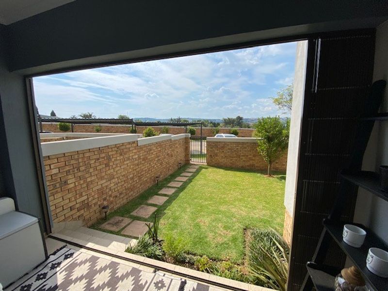 A view from an indoor space looking out onto a private garden area with a brick boundary wall and paved pathway.