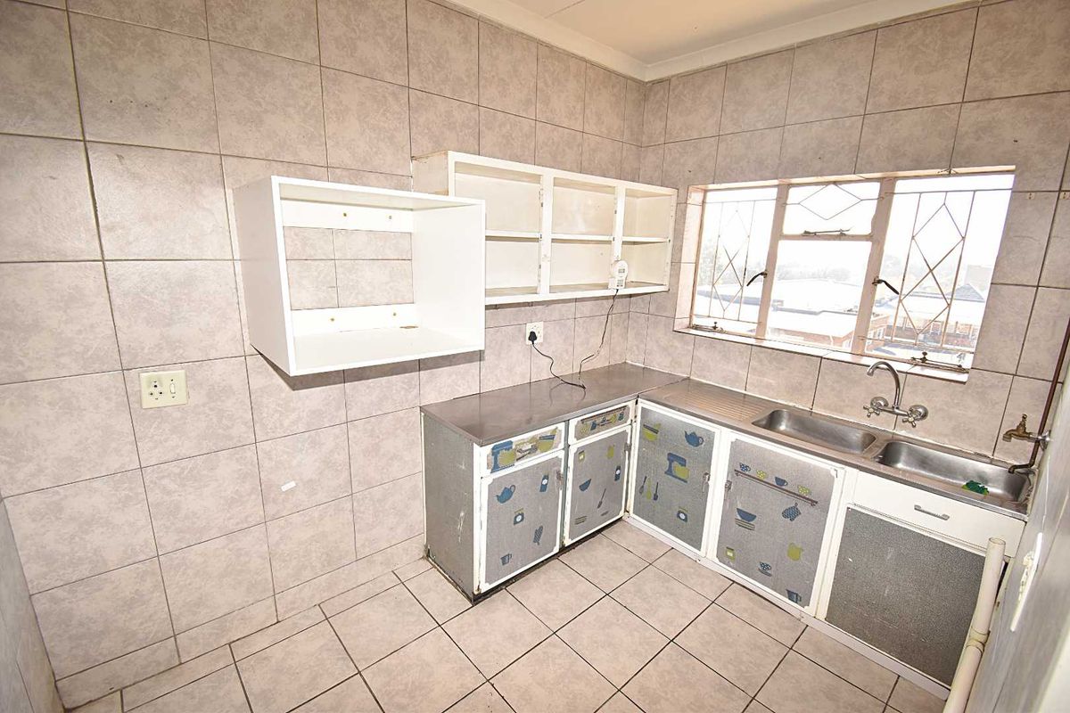 A dated kitchen featuring tiled walls and flooring, stainless steel sink, and basic cabinetry, offering a blank canvas for a modern renovation.