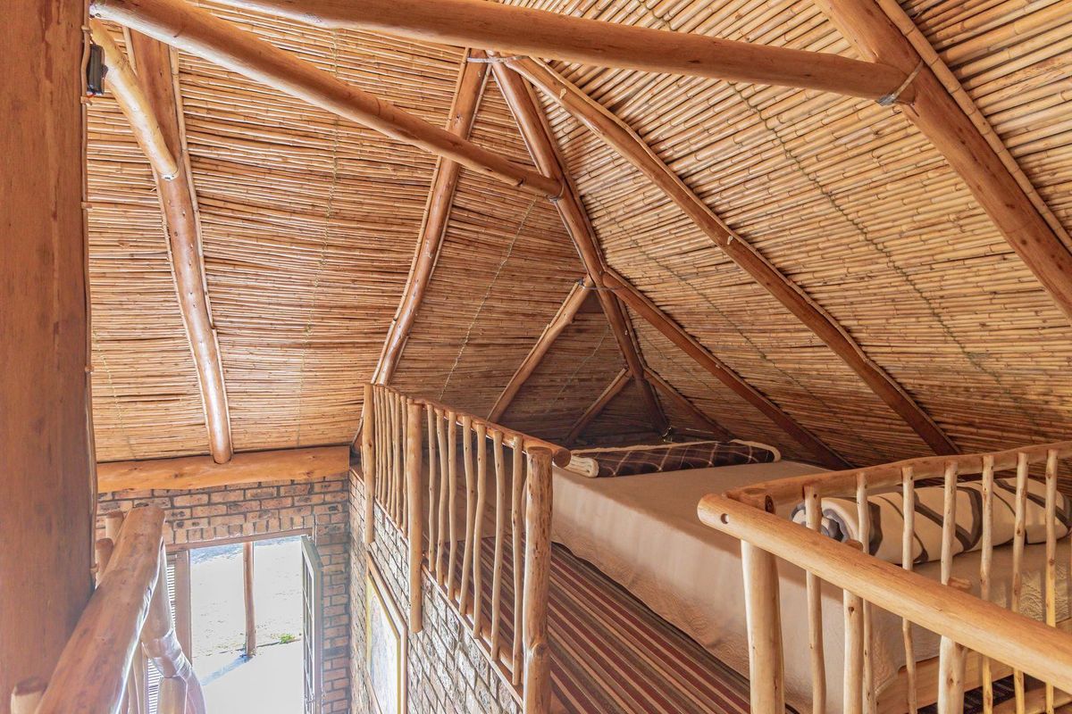 A rustic loft bedroom featuring a vaulted bamboo ceiling, exposed brick walls, and a wooden balustrade overlooking the lower level.