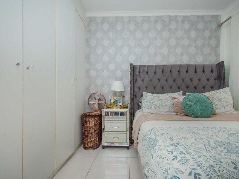 A well-maintained bedroom featuring built-in cupboards, tiled flooring, and a decorative feature wall with patterned wallpaper.