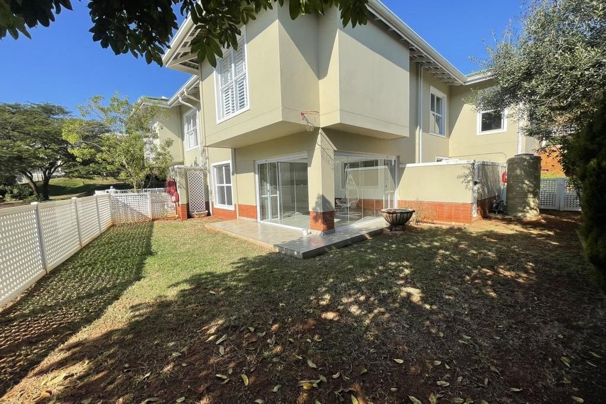 Rear view of the townhouse featuring an enclosed patio with sliding glass doors, a private garden area, and perimeter fencing.