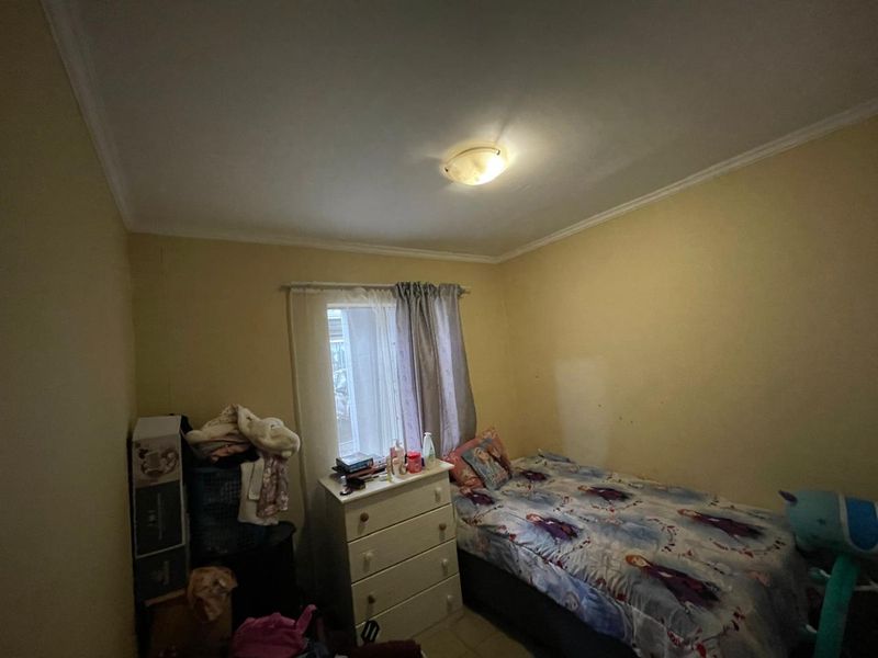 A compact bedroom featuring a central ceiling light and a window, currently requiring cosmetic updates to the wall finishes.
