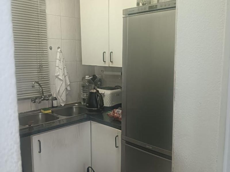 Compact kitchen featuring double sink, laminate countertops, and built-in cabinetry with tiled splashback, offering a functional layout in need of cosmetic updates.