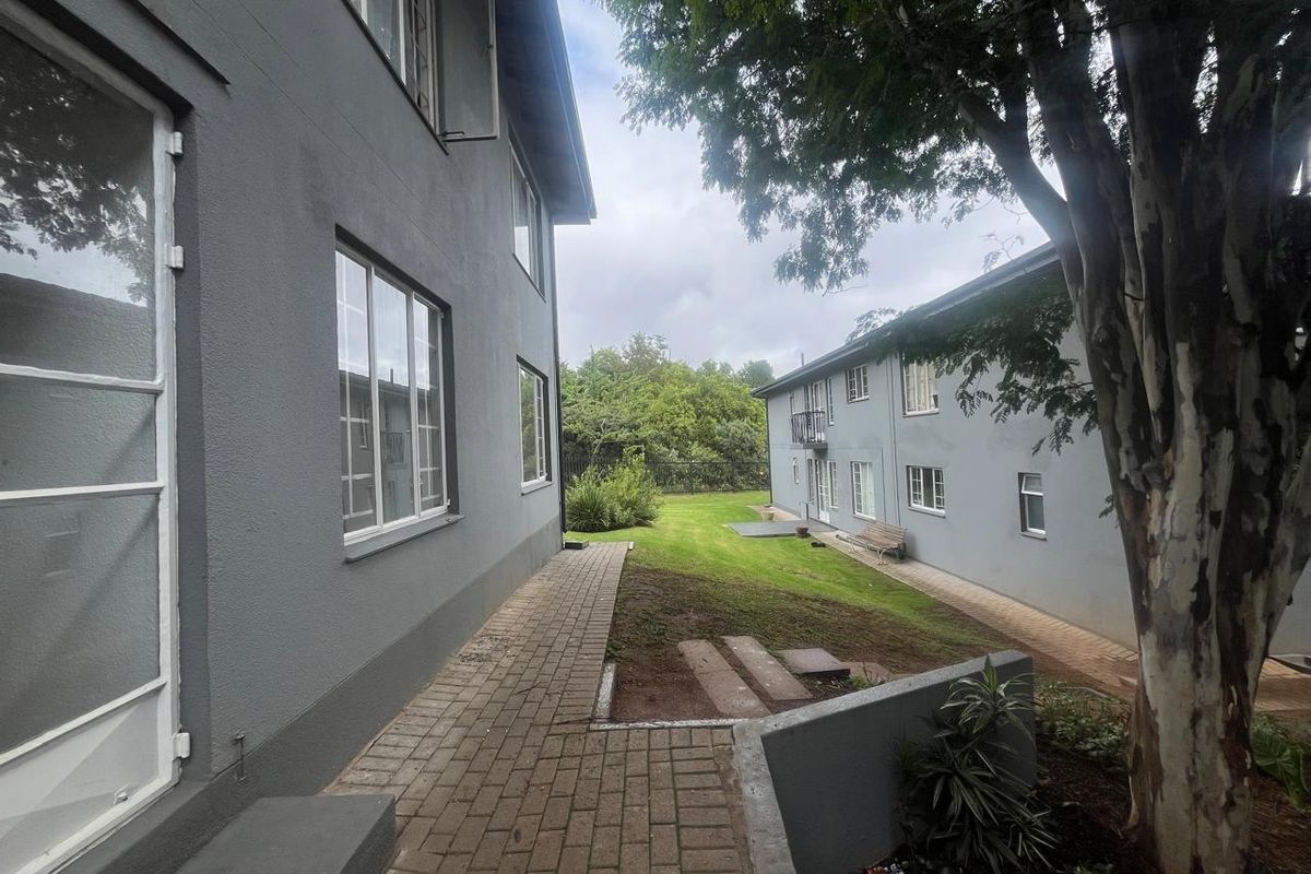 A view of the communal garden area between apartment blocks, featuring paved walkways and established trees.