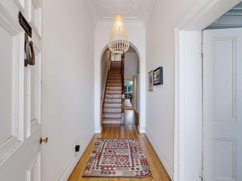 A welcoming entrance hallway featuring original timber flooring, a decorative pressed metal ceiling, and a classic timber staircase leading to the upper level.