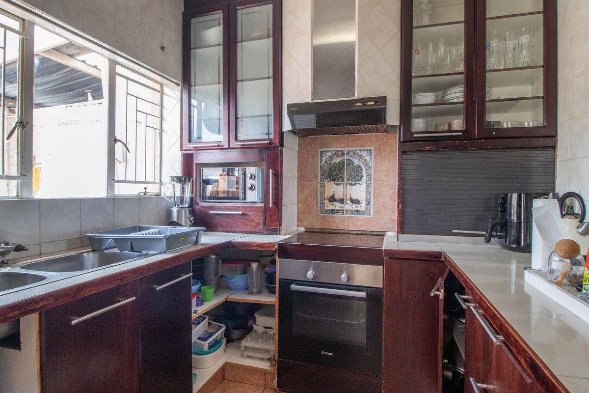A functional kitchen featuring dark wood cabinetry, a built-in oven, extractor fan, and a double stainless steel sink with tiled splashbacks.