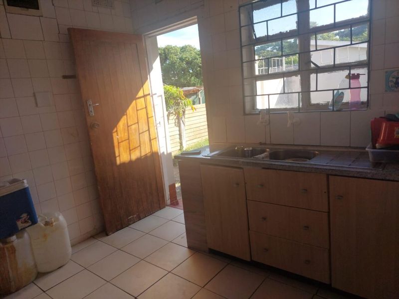 A functional kitchen area featuring tiled walls, built-in cabinetry, and a stainless steel sink, with direct access to the exterior.