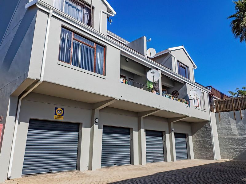 Exterior view of a multi-story apartment building featuring a paved driveway, four roller shutter garage doors, and an upper-level balcony.