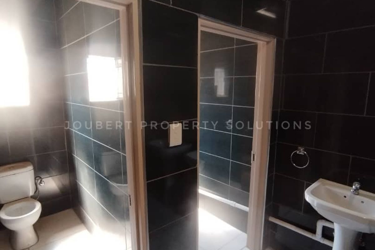 A functional bathroom facility featuring dark wall tiling, a pedestal basin, and a separate toilet cubicle.