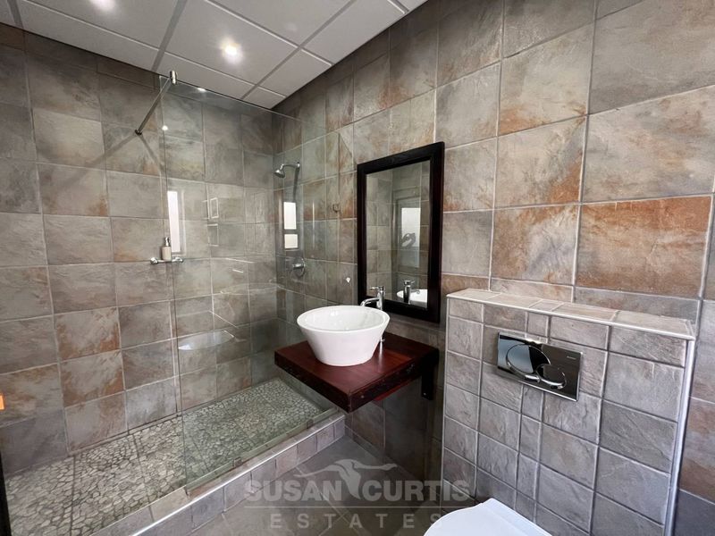 Modern bathroom featuring a walk-in shower with glass screen, vessel sink on a wooden vanity shelf, and a wall-hung toilet with concealed cistern.
