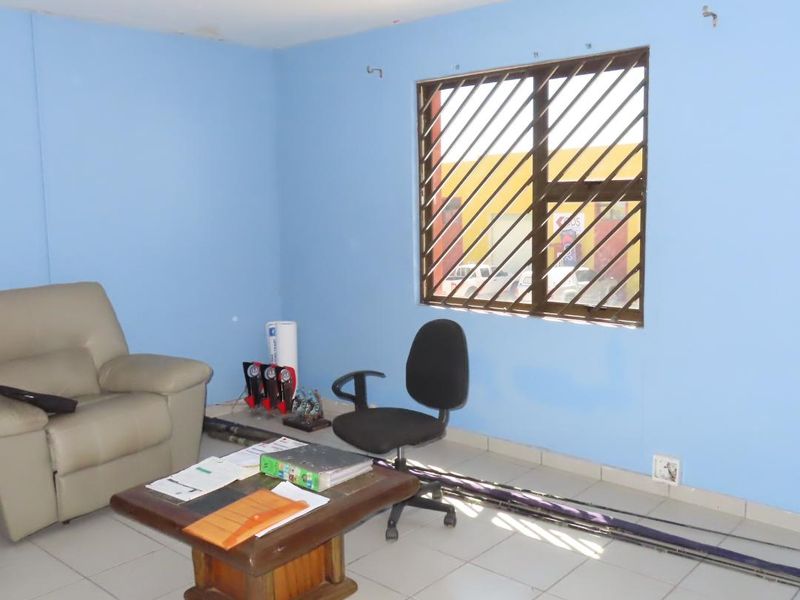 A functional office space featuring tiled flooring, a window with security bars, and blue painted walls, suitable for a professional workspace.