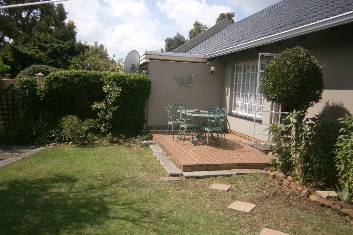 A rear exterior view of the townhouse featuring a tiled patio area, a well-maintained lawn, and established garden landscaping.