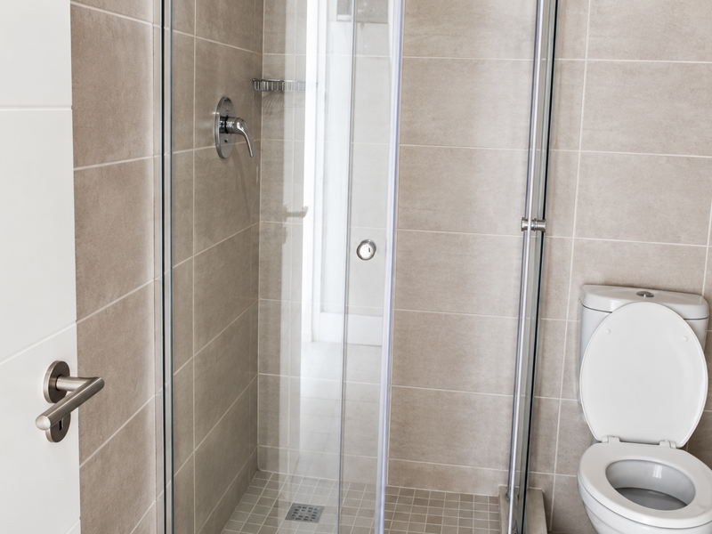 A modern bathroom featuring a glass-enclosed shower with chrome fixtures and a standard toilet, finished with neutral ceramic wall tiles and mosaic floor tiling.