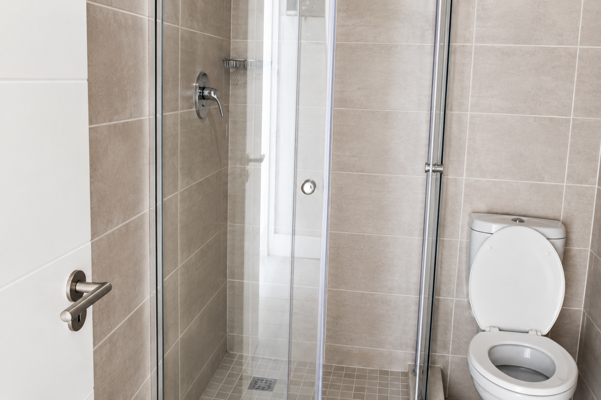 A modern bathroom featuring a glass-enclosed shower with chrome fixtures and a standard toilet, finished with neutral ceramic wall tiles and mosaic floor tiling.