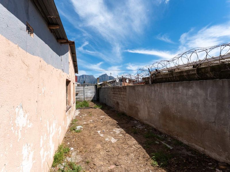 A narrow rear exterior passage featuring a perimeter wall with razor wire and significant wear to the building's exterior plaster finish.