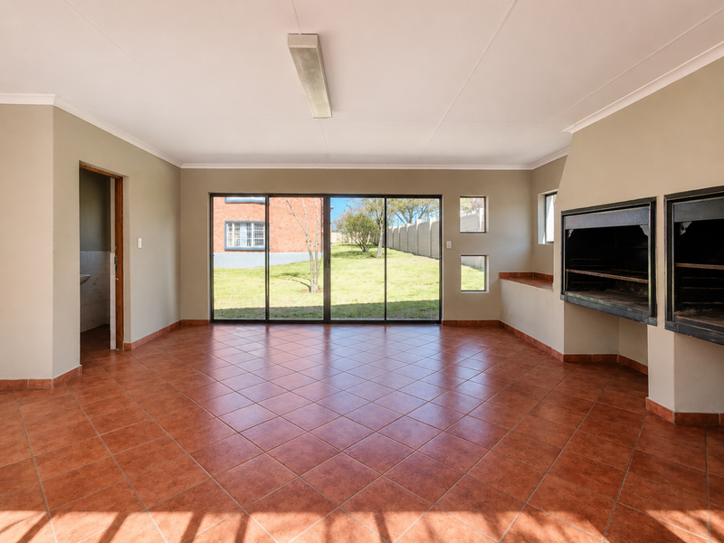Spacious living area featuring ceramic tile flooring, a built-in braai, and large sliding glass doors providing direct access to the garden.