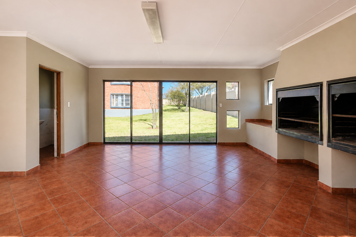 Spacious living area featuring ceramic tile flooring, a built-in braai, and large sliding glass doors providing direct access to the garden.