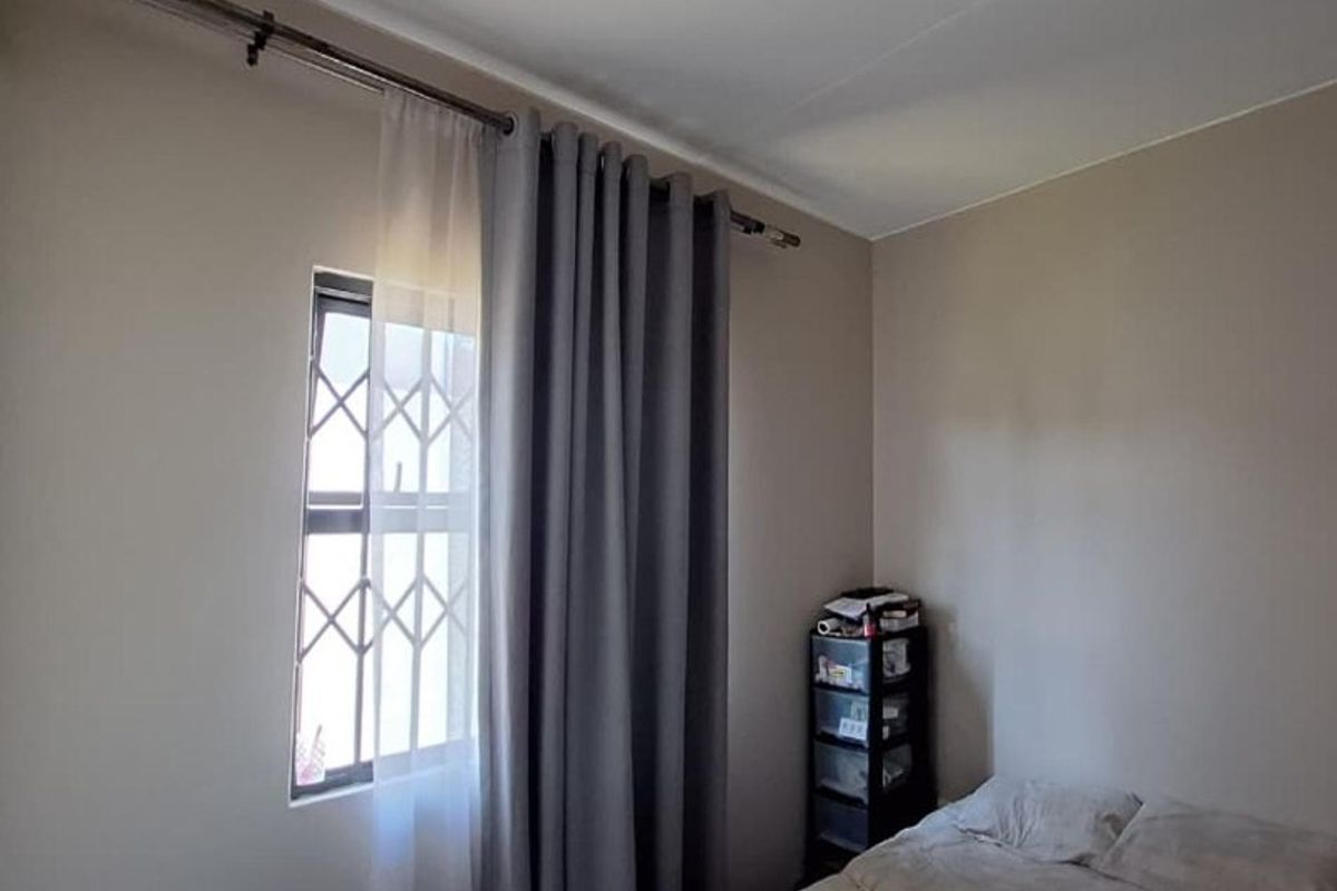A bedroom featuring a window with a fitted security gate and curtain rod, providing natural light and basic security.