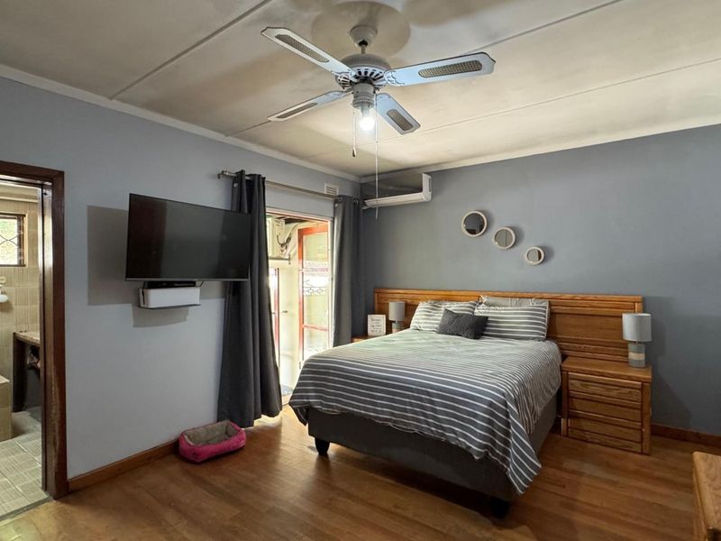 A well-maintained bedroom featuring laminate flooring, a ceiling fan, and a split-system air conditioner, with an adjoining en-suite bathroom.