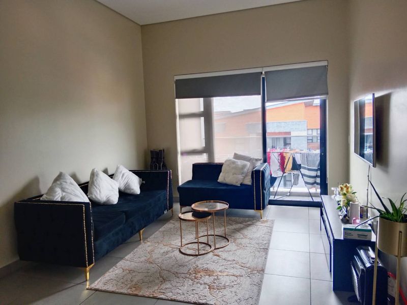 A well-lit living room featuring neutral tiled flooring and a large sliding glass door that provides access to an outdoor balcony area.