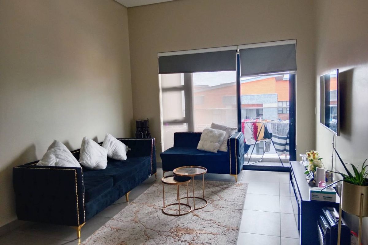 A well-lit living room featuring neutral tiled flooring and a large sliding glass door that provides access to an outdoor balcony area.