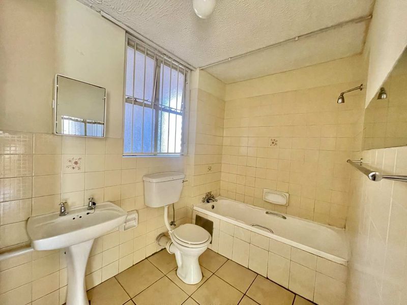 A dated bathroom featuring a pedestal basin, toilet, and bathtub with tiled walls and flooring, requiring modernization to improve its overall condition.