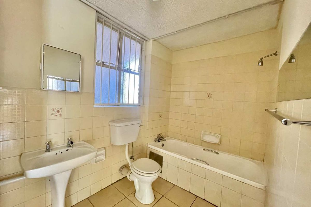 A dated bathroom featuring a pedestal basin, toilet, and bathtub with tiled walls and flooring, requiring modernization to improve its overall condition.