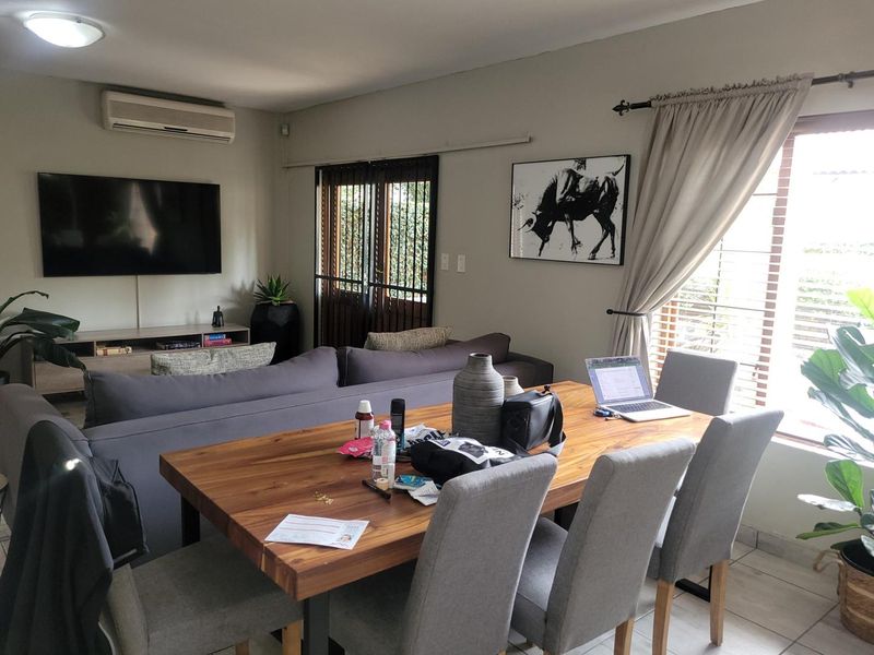 Open-plan living and dining area featuring tiled flooring, a wall-mounted air conditioning unit, and security gate access to the exterior.
