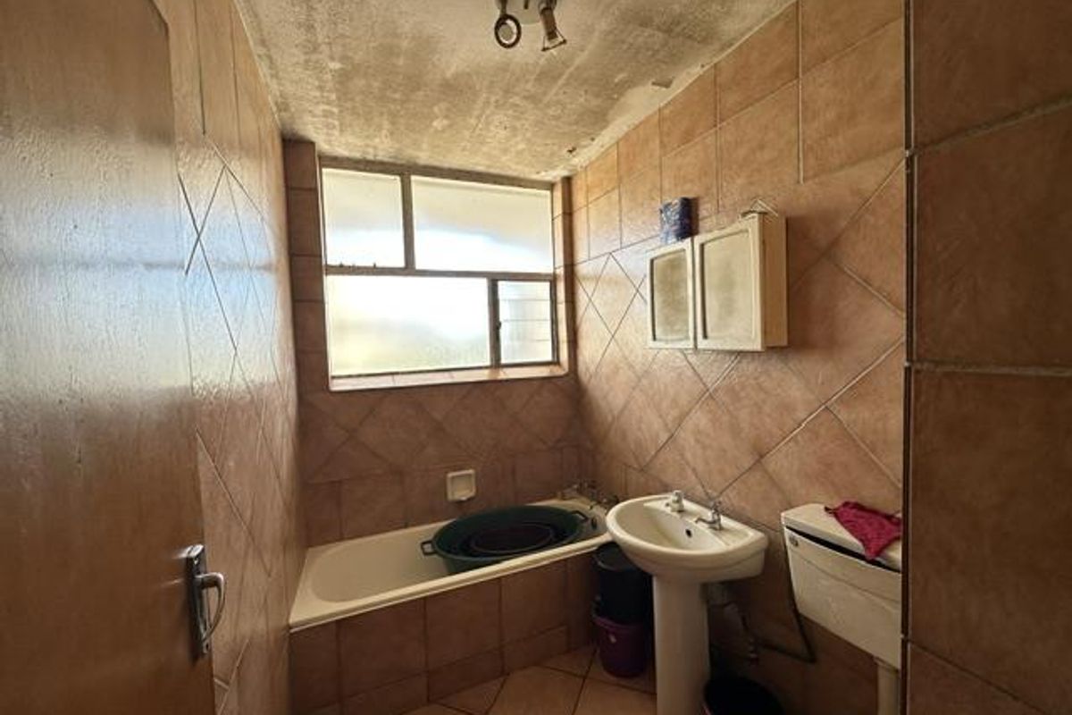 A dated bathroom featuring a pedestal basin, toilet, and bathtub with full-height wall tiling and a window for natural light.