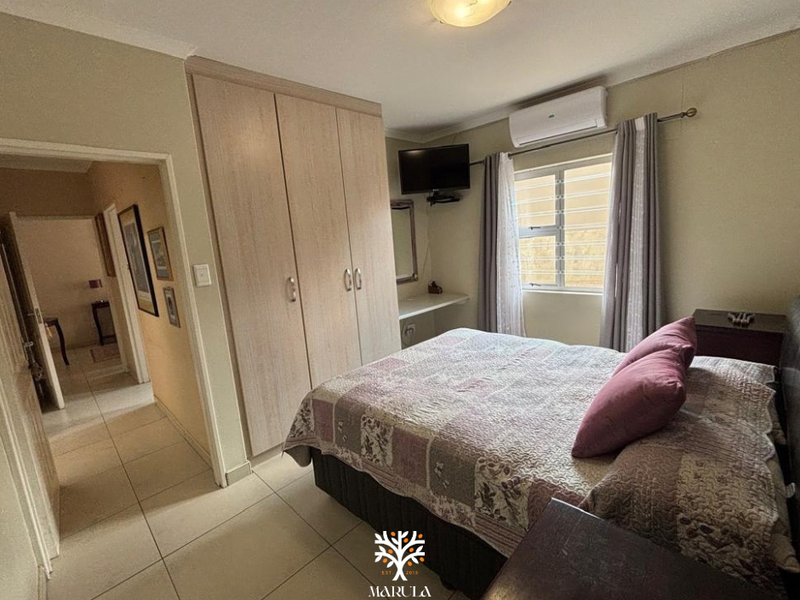A functional bedroom featuring built-in cupboards, tiled flooring, and an air conditioning unit, providing a comfortable and practical living space.