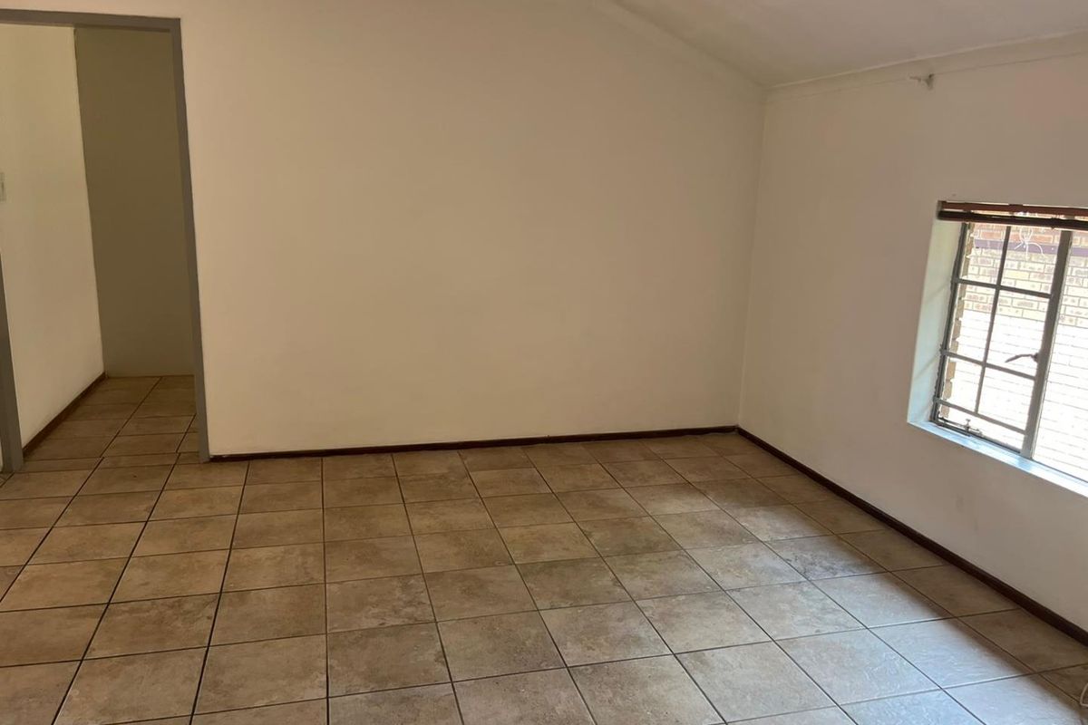 An empty bedroom featuring neutral walls, tiled flooring, and a window with security bars.