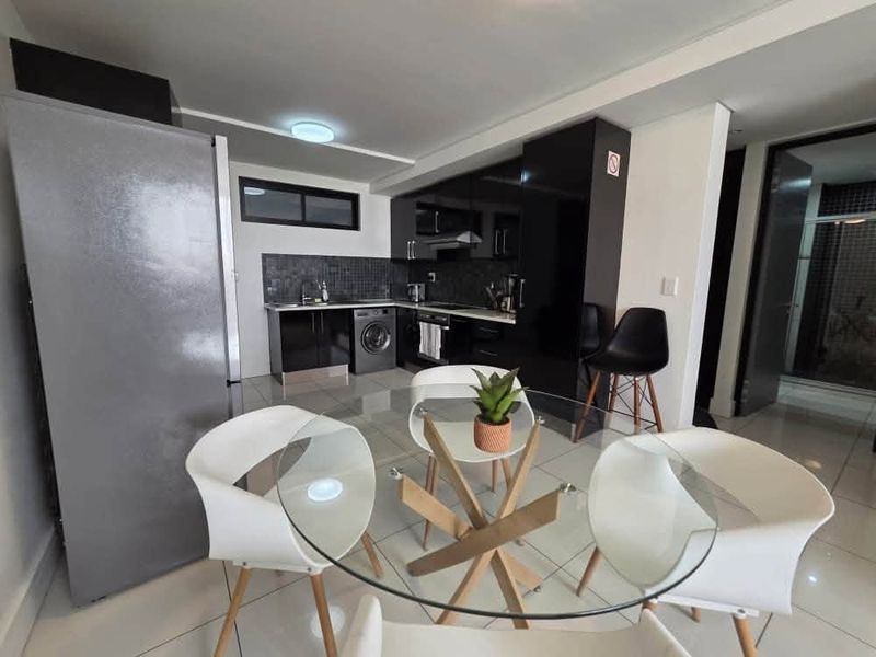 Modern open-plan kitchen featuring sleek black cabinetry, tiled flooring, and integrated appliances, seamlessly flowing into the dining area.