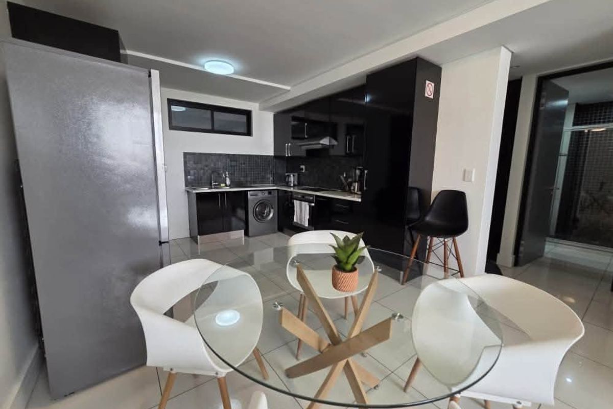 Modern open-plan kitchen featuring sleek black cabinetry, tiled flooring, and integrated appliances, seamlessly flowing into the dining area.