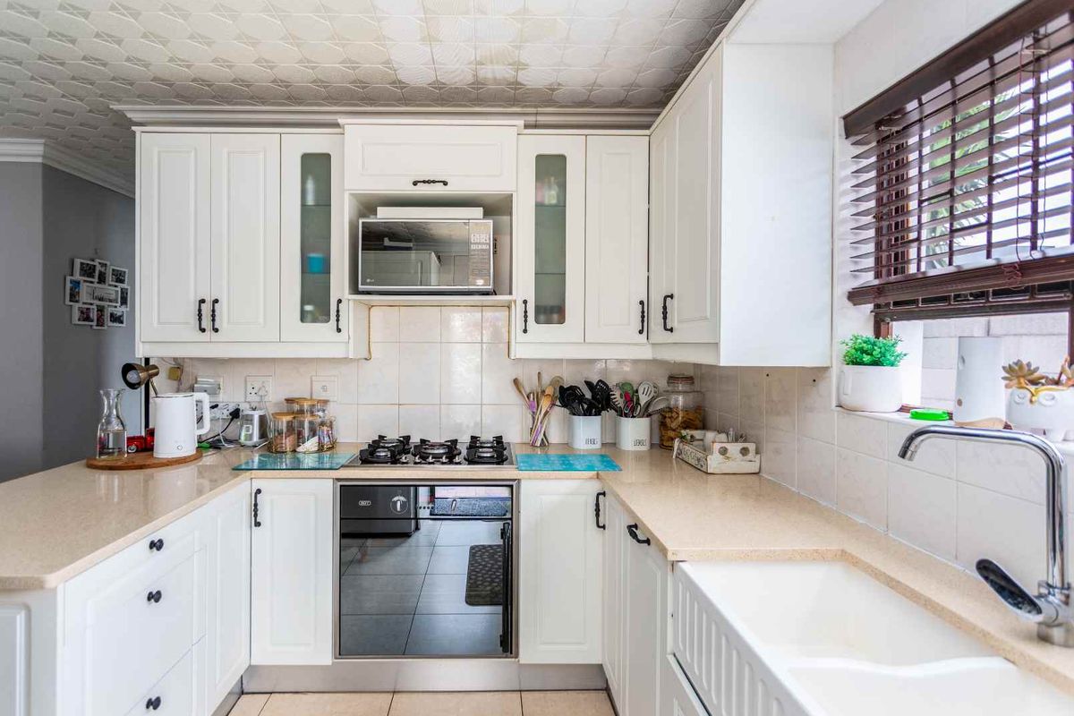 A well-maintained kitchen featuring white cabinetry, integrated oven and hob, stone-look countertops, and a farmhouse-style sink with a tiled backsplash.