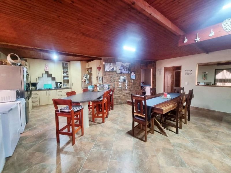 Spacious open-plan living and dining area featuring a large kitchen island, stone feature wall, and exposed timber ceilings with tiled flooring throughout.