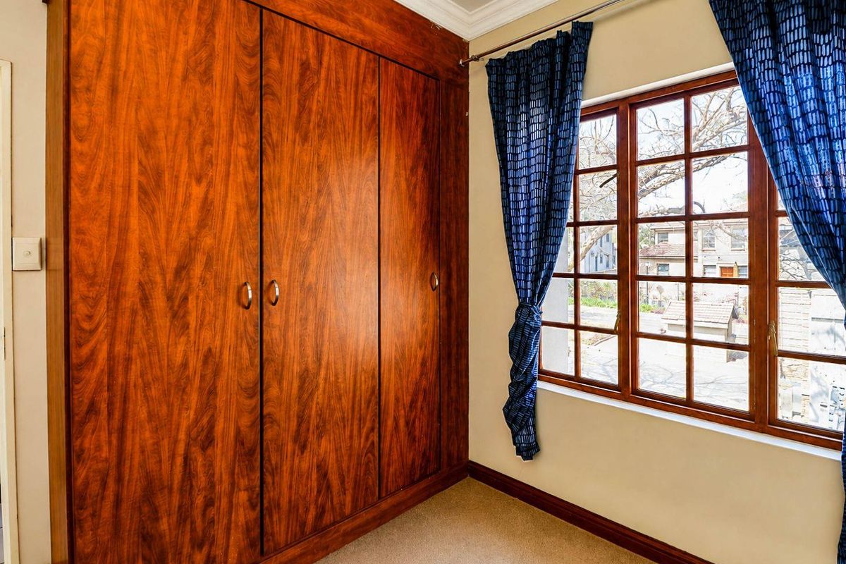 A bedroom featuring a large built-in wooden wardrobe, timber-framed window, and neutral carpeting.